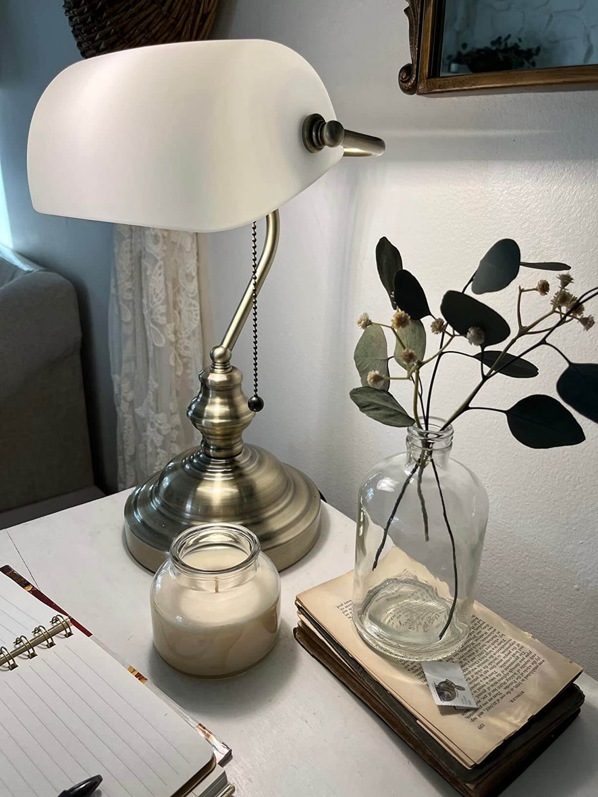 White Matted Glass Banker Lamp on a bedside table with a candle and decorative plants.