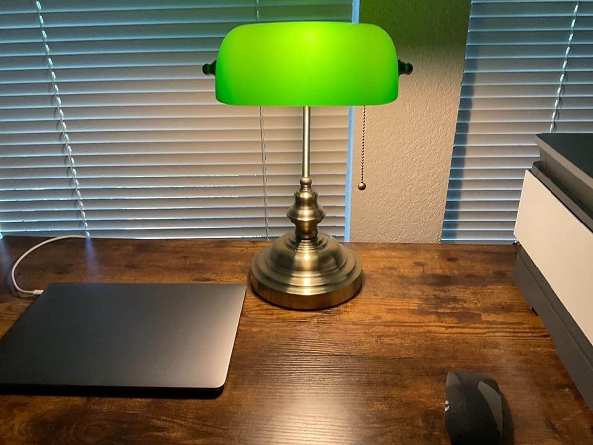 Green Glass Banker Desk Lamp with Pull Chain Switch on a wooden desk near a laptop.