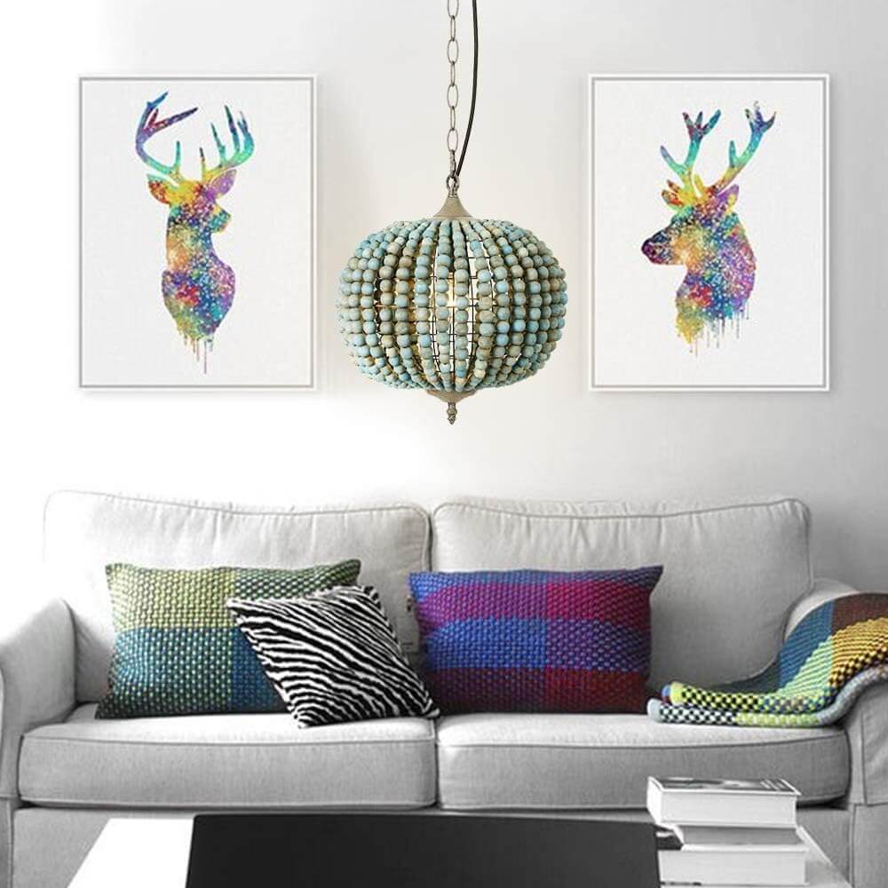 Blue Wood Bead Globe Pendant Light hanging over a cozy sofa with colorful pillows and artistic deer wall art.