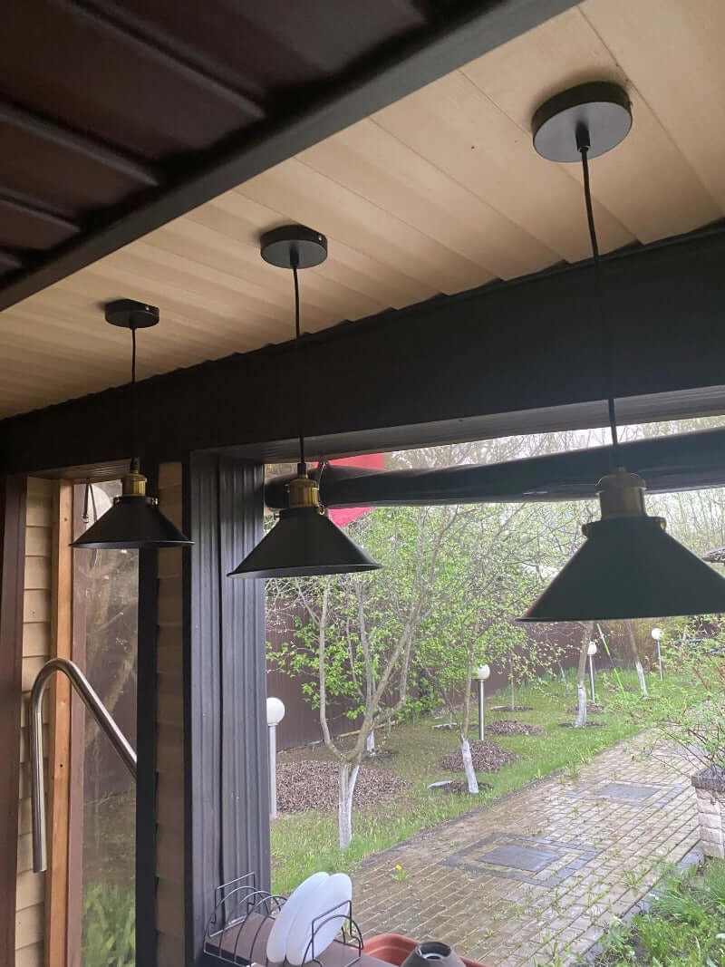 Industrial Retro Black Iron Pendant Light,2 Pack hanging in a bright indoor setting with gardens visible outside.