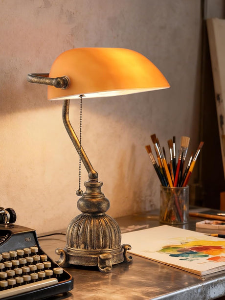 Newrays retro amber glass desk lamp illuminating workspace with typewriter and brushes in background.